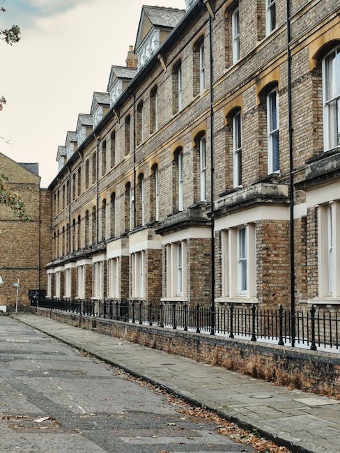 An exterior view of a row of traditional brick residential flats located on Fulham Road, with a narrow sidewalk in front. The buildings feature multiple stories, each with white-framed windows and decorative stone lintels. The brickwork shows signs of weathering, and the pavement along the sidewalk has some fallen leaves and minor debris, indicating the need for surface cleaning and maintenance. The scene is illuminated by natural daylight, highlighting the textures of the brick and stonework. This image relates to domestic cleaning services offered by Cleaners SW10, focusing on maintaining and revitalising exterior surfaces of residential properties in the SW10 area, including thorough surface cleaning and exterior sanitisation, aligning with their end of tenancy cleaning for flats on Fulham Road.