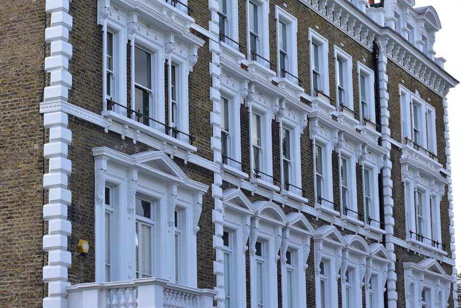 Exterior view of a traditional multi-story residential building on Fulham Road, featuring detailed white architectural mouldings around the windows and along the façade. The building's brickwork is dark brown, contrasting with the ornate white trim, window frames, and decorative cornices that highlight the classical design. Sunlight illuminates the façade, emphasizing the cleanliness and well-maintained appearance of the exterior surfaces, with no visible dirt or damage. The windows are clear and shimmering, suggesting recent surface cleaning or regular maintenance. This image reflects the type of high-quality, detailed property that Cleaners SW10 can assist with through professional domestic cleaning and surface care services, such as deep cleaning, surface sanitisation, and window cleaning, tailored for properties in the SW10 Fulham area.